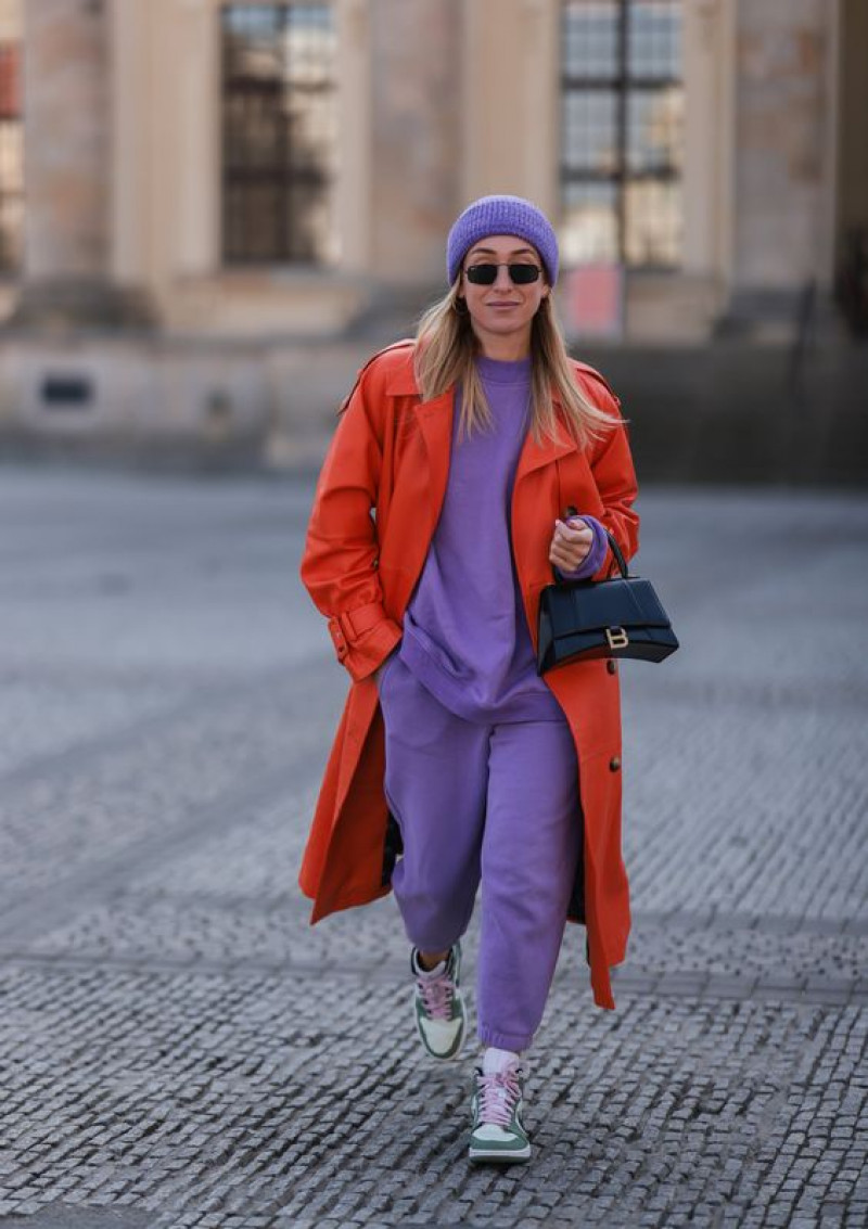 Bold Orange Trench with Lavender Tracksuit and Pastel Sneakers: orange trench coat,  purple and violet jeans,  grey sneaker,  grey trainer,  orange and purple and violet,  orange trench coat and purple and violet jeans  